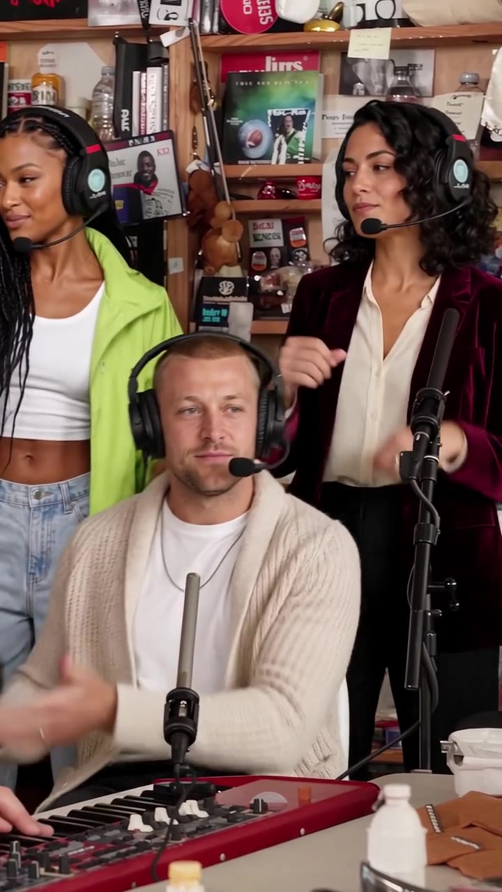 Tiny Desk AI still: a lead singer in a burgundy blazer sings into a headset mic in front of a crowded bookshelf